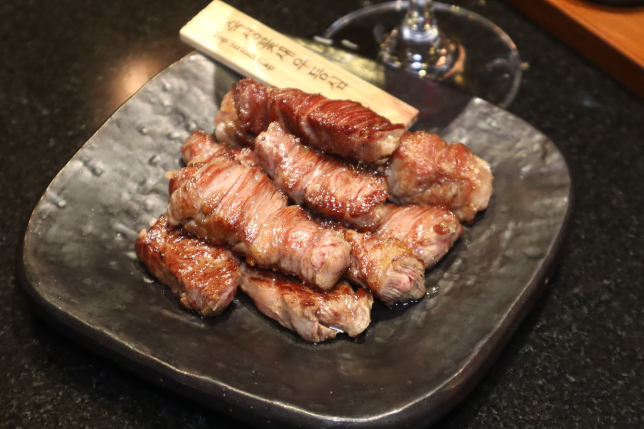 Grilled top sirloin cap glistening on a dark plate